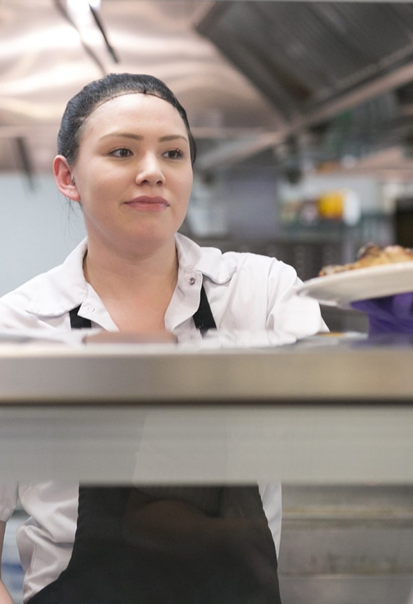 A girl behind a counter warmly serving delicious food.